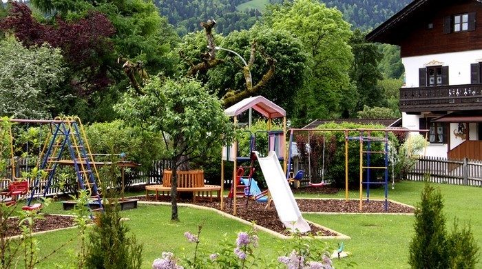A playground for kids with swings and a slide in the yard of a house.