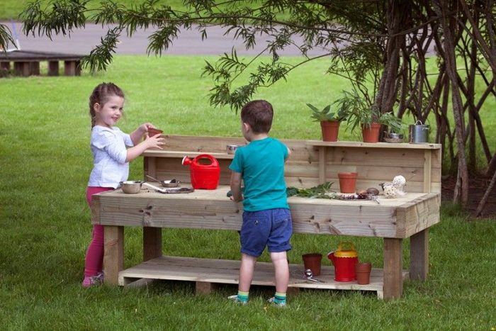 Two kids enjoy a wooden play table in a playground designed for kids.