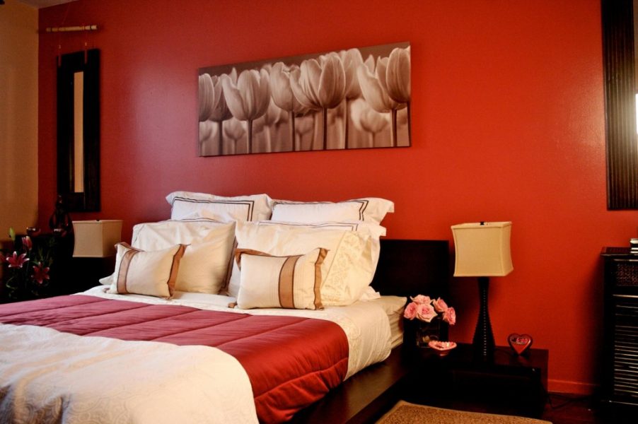 A bedroom with vibrant red walls and a crisp white bed.