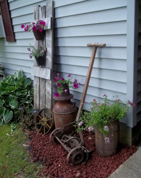 An old wheelbarrow and flower pots in a small space on the side of a house.
