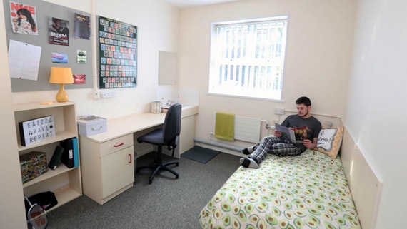 A man sitting in a small university dormitory room.