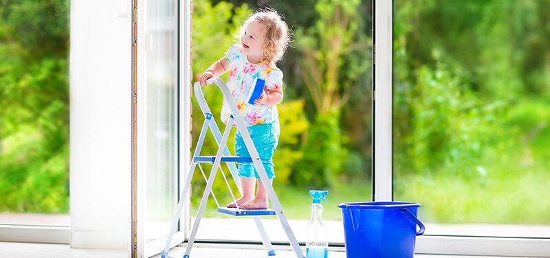 A little girl cleaning windows while standing on a ladder.