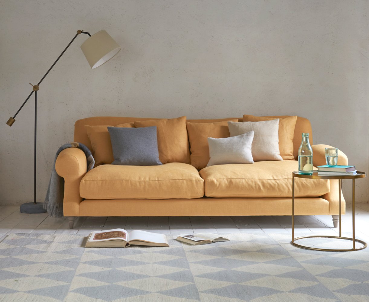 A living room with a yellow sofa and a grey rug featuring trade furniture.