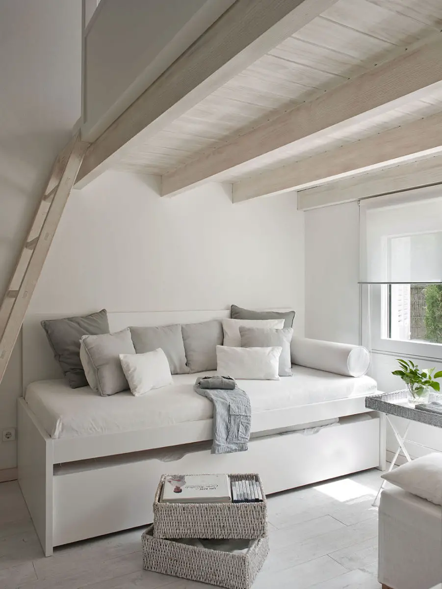 A white bedroom in a house with a day bed and a stairway.