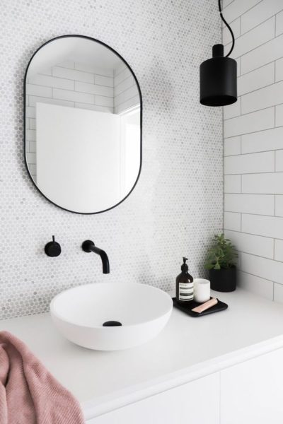 A small black and white bathroom with a pink towel and a round mirror.