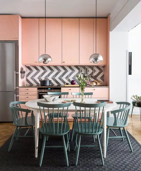 Modern kitchen with pink cabinets and teal chairs.
