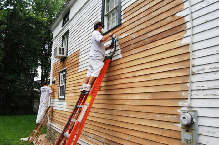 Two men painting a home's wood siding.