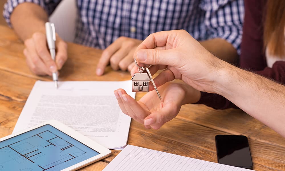 A person holding a key to a property while holding a tablet for property investment purposes.