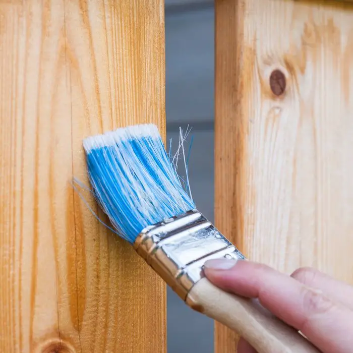 A person is renovating a wooden fence with a paint brush.