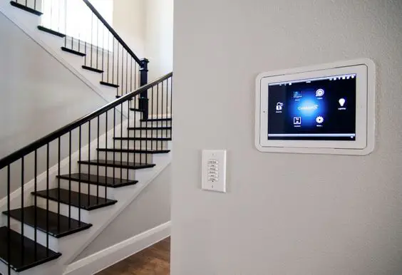 A smart home security system is mounted on the wall next to the stairs.