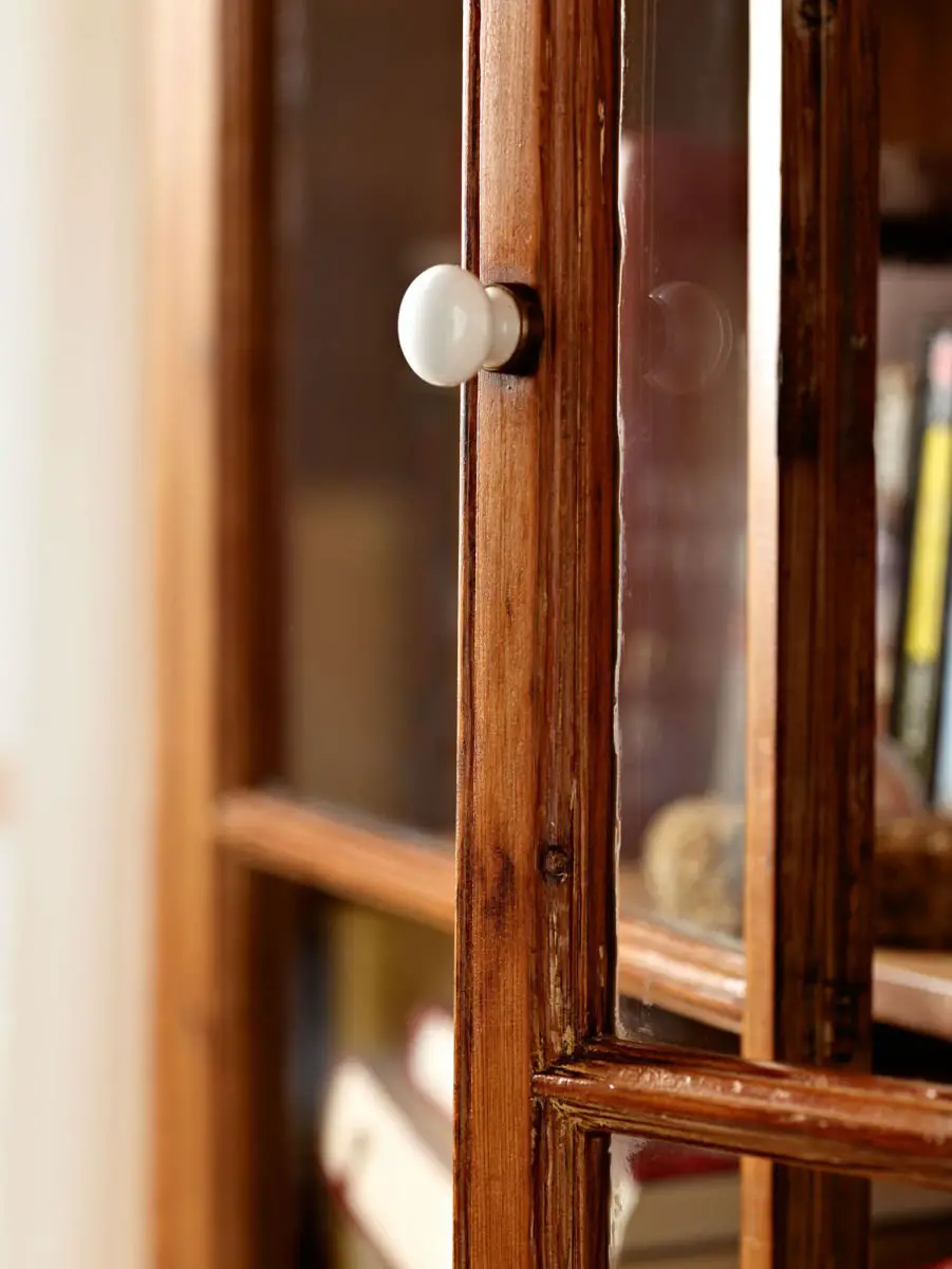 A wooden bookcase with a glass door and a knob that is susceptible to woodworm.