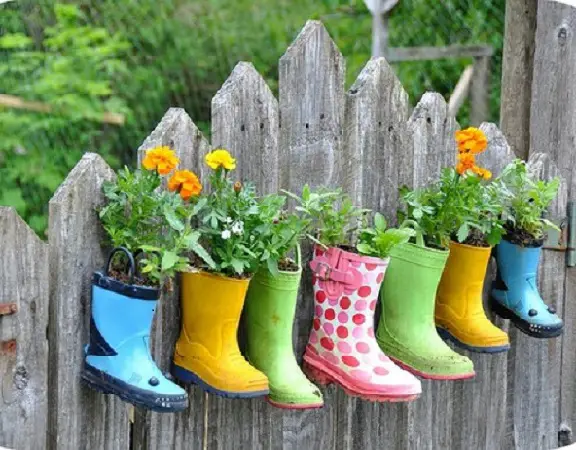 A group of colorful rain boots hanging in a garden.