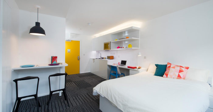 A student room with a bed, desk and yellow door.