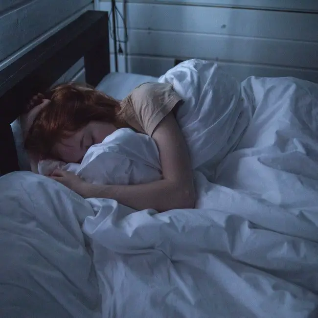 A woman sleeping in a white sheeted bed in her bedroom.