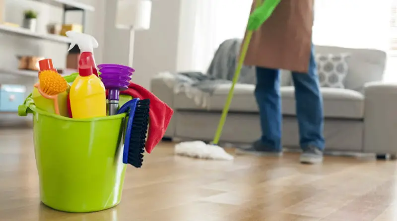 A man tidying up a living room with cleaning supplies, ensuring a spick and span home.