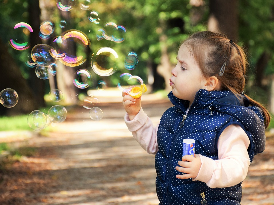 A little girl with kids blowing soap bubbles in the park.