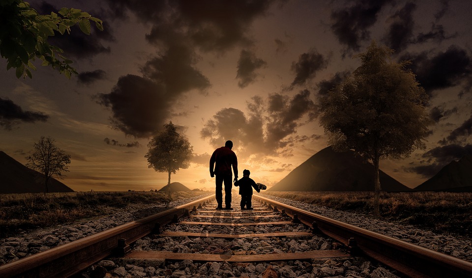 A man and a child moving on train tracks at sunset.