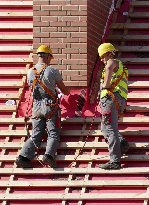 Two construction workers installing metal roofing on a roof.