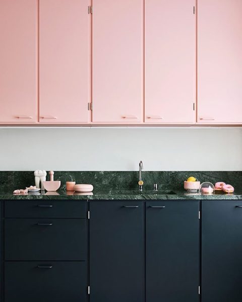 A kitchen with pink cabinets and black counter tops, utilizing the color pink.