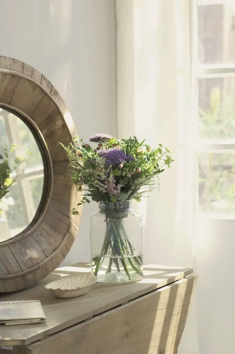 A vase of flowers sits on a renovated wooden table in front of a mirror.