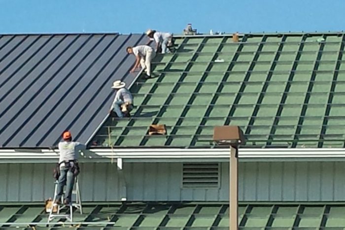 A group of men installing metal roofing on a building.
