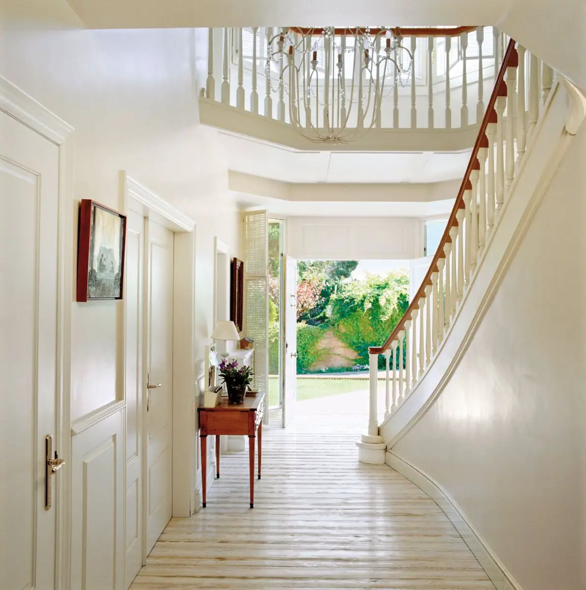 A hallway with natural light, a white staircase, and chandelier.