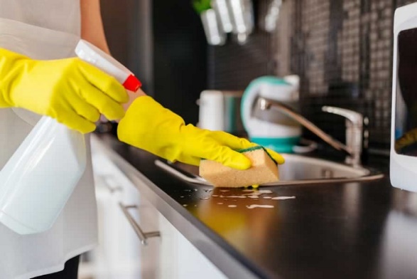 A woman in yellow gloves cleaning a kitchen counter with remodeling ideas in mind.