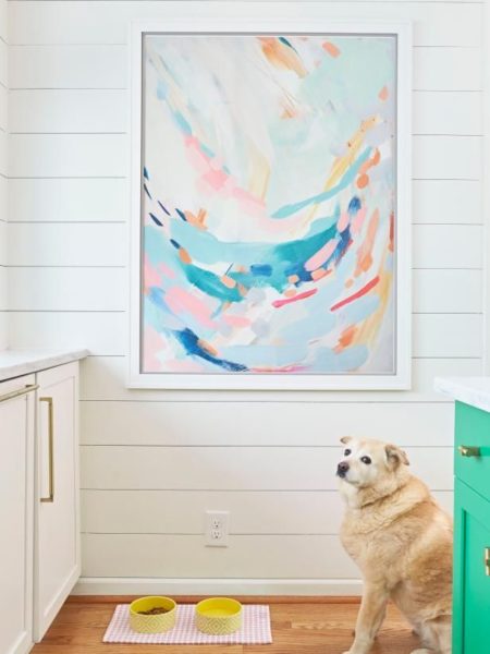 A dog standing in front of a painting in a kitchen in a living room.