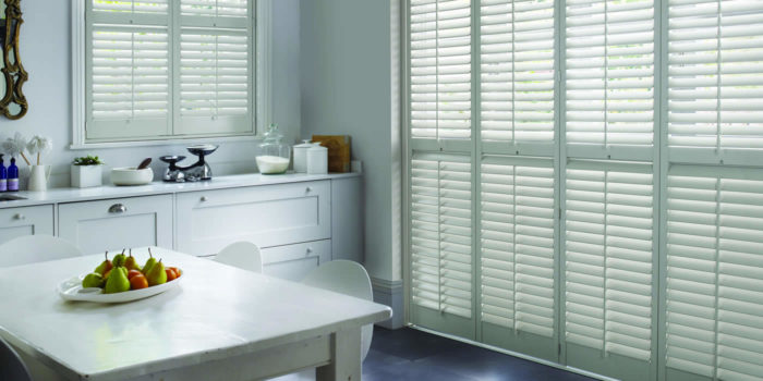 White shutters in a kitchen with window treatments.
