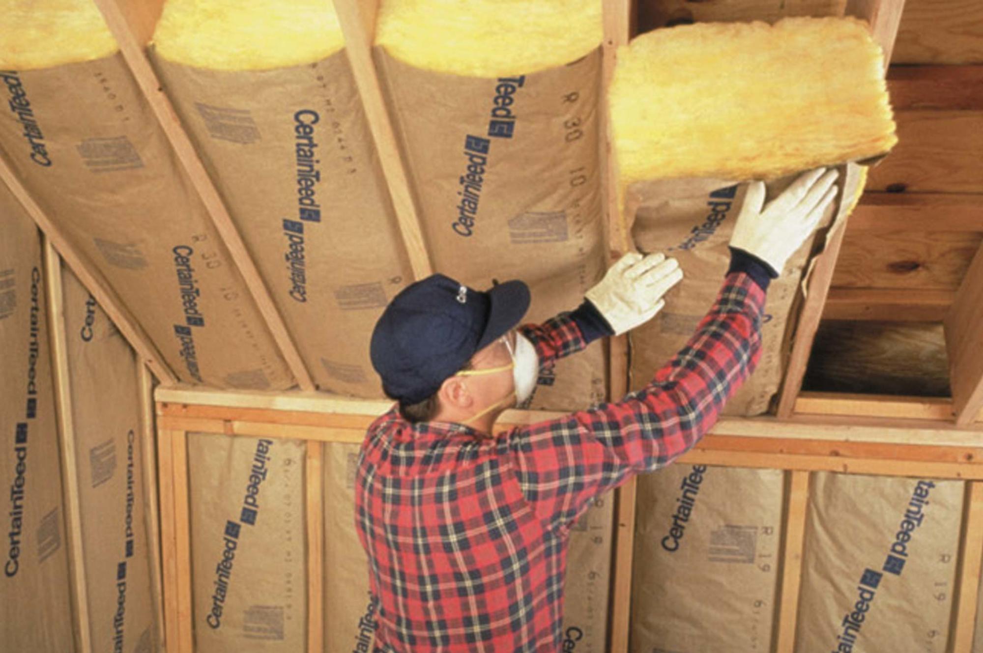 A man is installing fiberglass insulation in an attic.