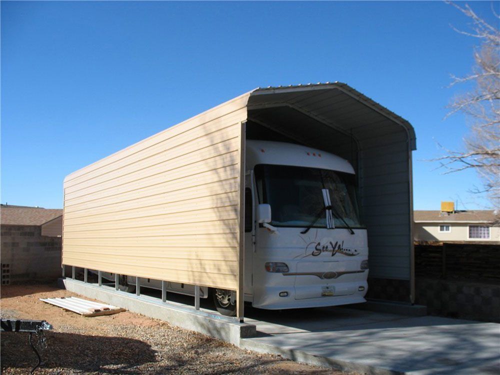 A tan rv parked in a home garage shelter.