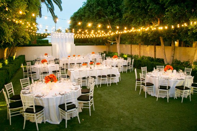 An outdoor backyard wedding reception set up with white tables and chairs.