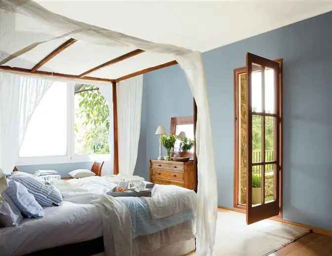 A renovated bedroom with blue walls and a white canopy bed.