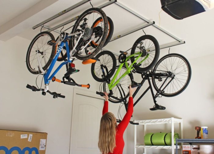 A woman is using clever garage ideas to put her bicycles on a rack in a garage.