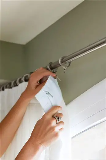 A woman is renovating a window by installing a curtain rod.