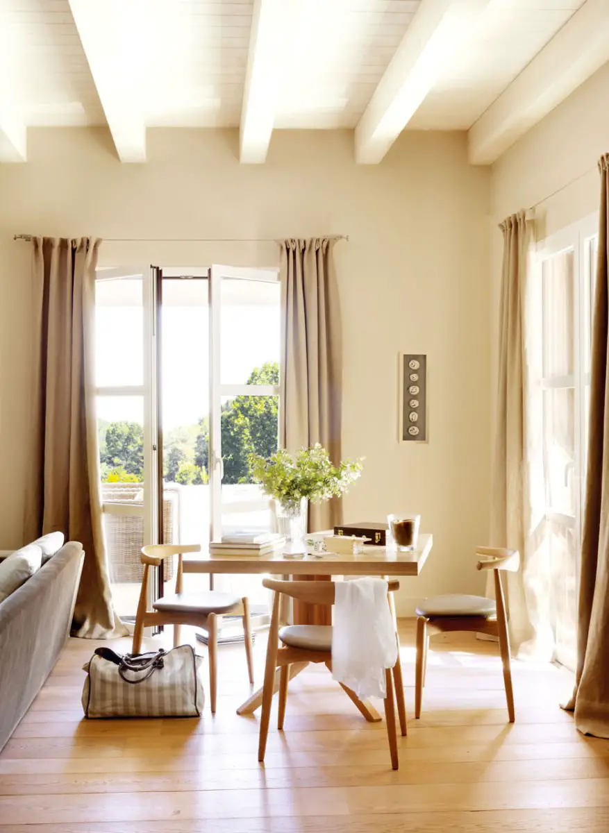 A living room with beige walls, wooden floors, and curtains.