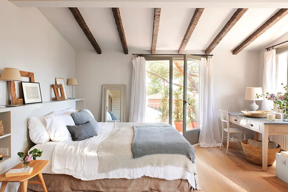 A bedroom with wooden beams, a white bed, and curtains.