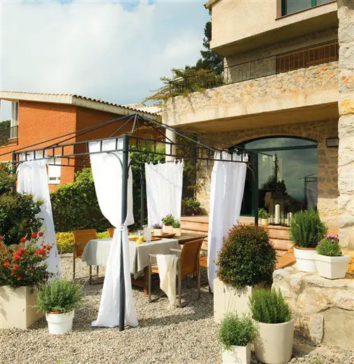 A renovated outdoor dining area with white curtains and potted plants.