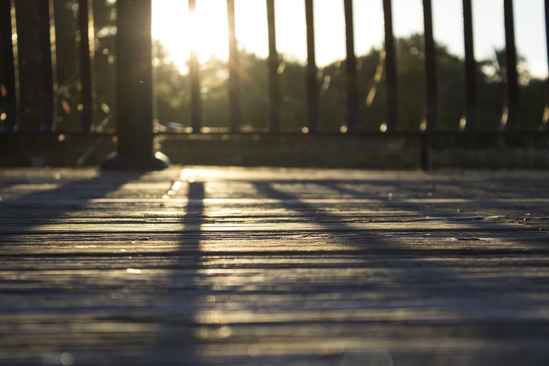 A person's shadow on a wooden deck needing repair.