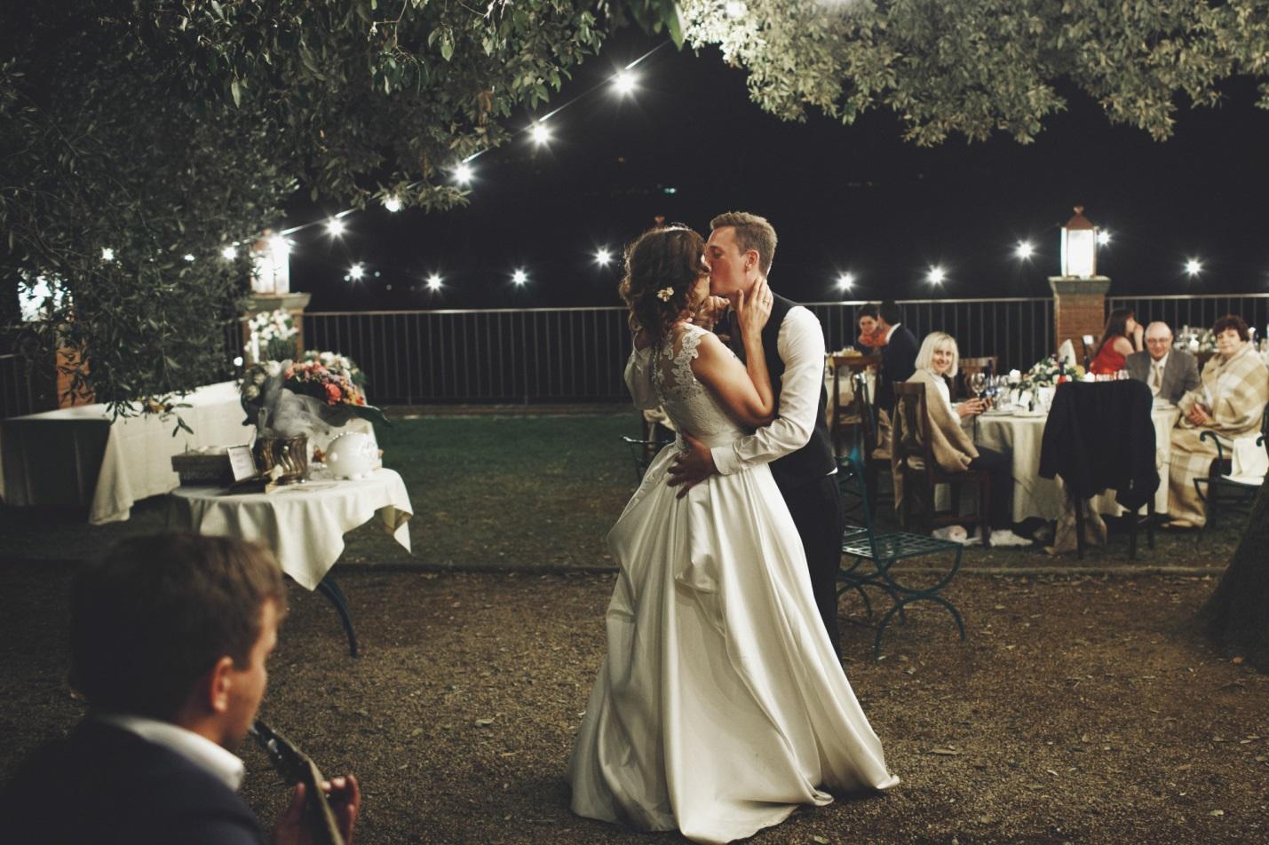 A bride and groom sharing their first dance in a backyard garden at night.