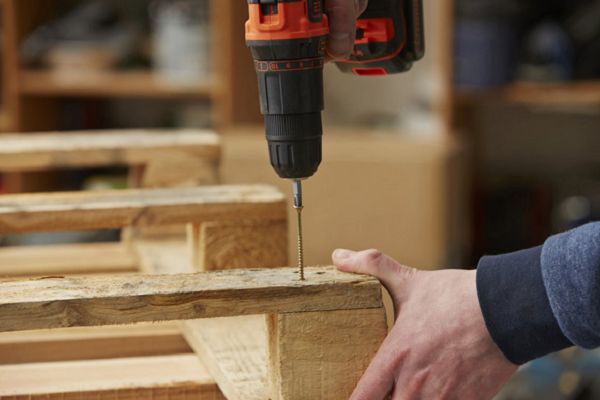 A person using a drill on wooden pallets.