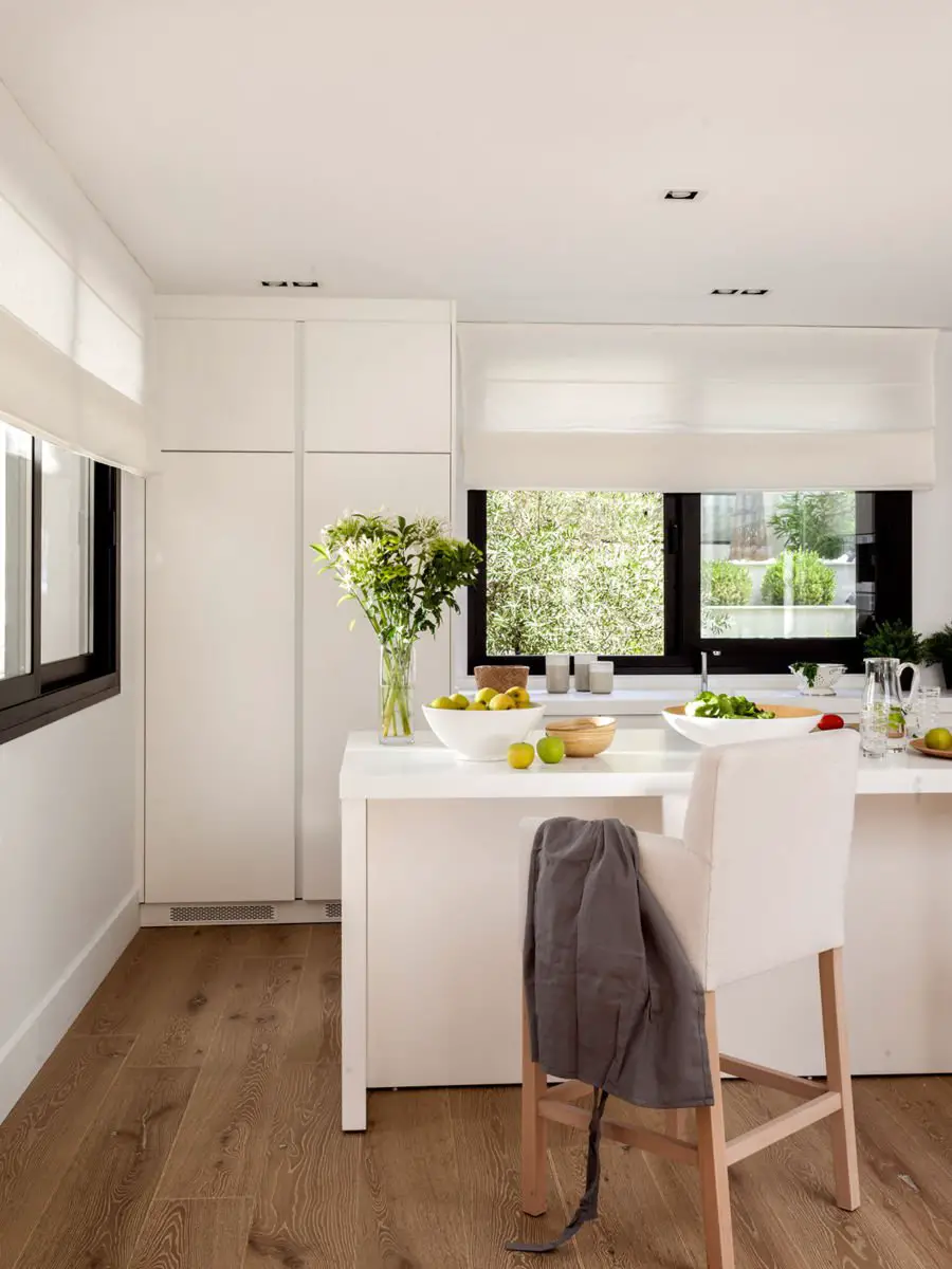 A white kitchen with wooden floors and curtains.