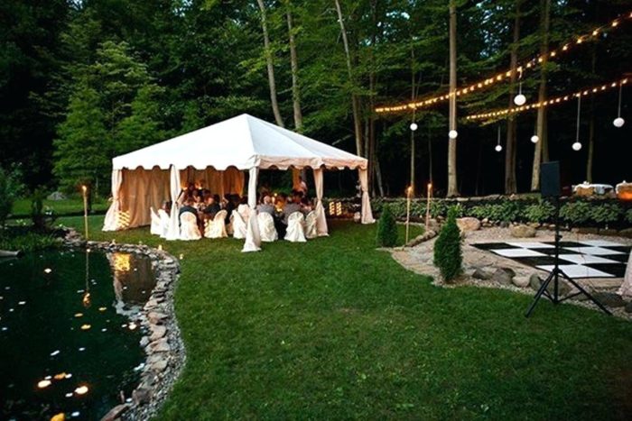 A white tent is set up near a pond for a backyard wedding.