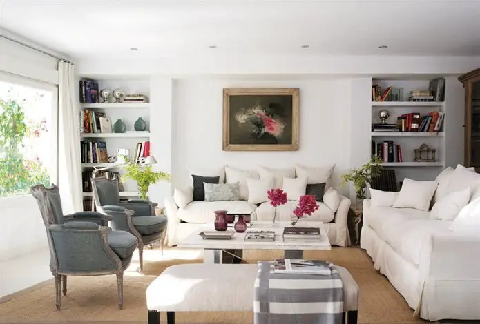 A white furniture-filled living room in a home with bookshelves.