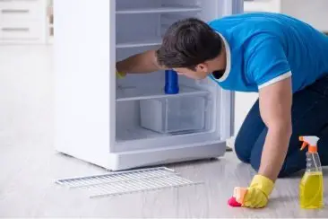 A man cleaning the inside of a house refrigerator.