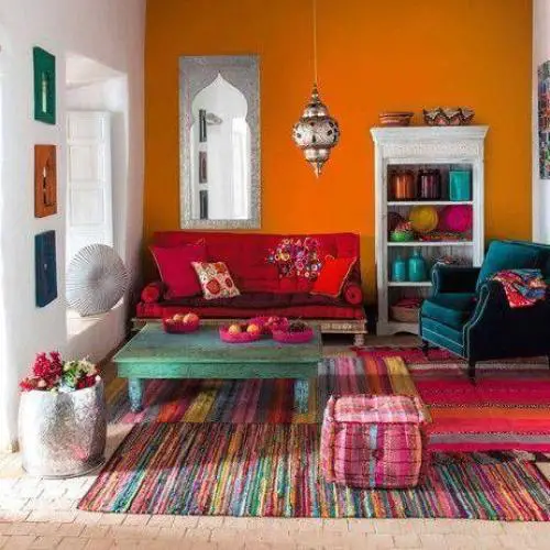 A boho chic living room with colorful furniture and orange walls.