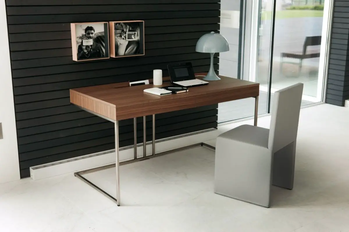 A modern desk made of wooden furniture in a room with black walls.