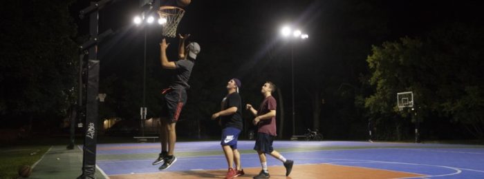 A group of people playing basketball on a court with external LED lighting.