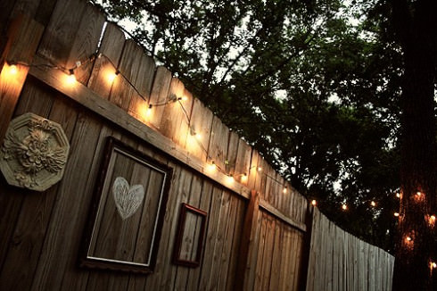 A wooden fence is lit up with string lights to properly light your back deck.