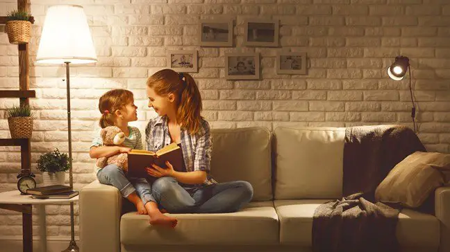 A mother and daughter cozy at home reading a book.